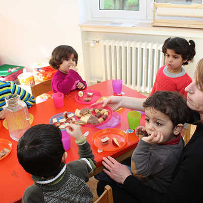 Im Burgunderviertel lernen Kleinkinder in der Kinderstube des Deutschen Roten Kreuzes die deutsche Sprache und Kultur kennen. Das Angebot ermöglicht es ihren Eltern, währenddessen einen Deutschkurs zu besuchen. Hier geht es oft laut und fröhlich zu. Damit die Kinder wieder zu Kräften kommen, reicht Pädagogin Alexandra Marx (r.) zwischendurch kleine Stärkungen. 