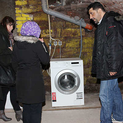 Die städtische Sozialarbeiterin Franziska Fischer (l.) und der Sprachmittler Ayad Abbas von der Caritas erklären einer jungen Syrerin, wie sie die Waschmaschine bedienen soll.