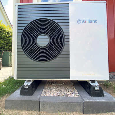 Eine Luftwärmepumpe steht auf einem Sockel vor einem Wohnhaus.