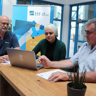 Der technische Direktor Lothar Simon (l.) und Vorstand Rainer Schramm von ttt-it AG besprechen mit der aus Syrien stammenden Auszubildenden Alaa Jouri Ergebnisse einer Übungsaufgabe in der IT-Anwendungsentwicklung. Foto: Jobcenter/tas