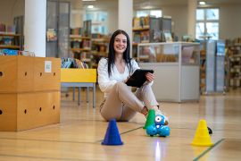 Junge Frau steuert in der Bibliothek mit einem Tablet einen kleinen Roboter