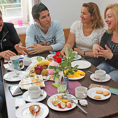 Bei Heißgetränken, frischem Obst und Kuchen erzählen die Syrerinnen und Syrer Helferin Ida (rechts)  von ihren Zukunftsplänen. Dabei wird auch viel gescherzt und gelacht. 