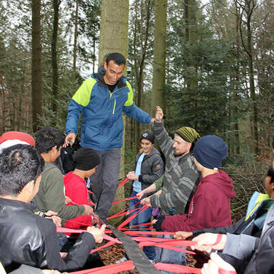 Im Weisshauswald befestigen die Erlebnispädagogen ein langes Gurtband an einem Baum, das die Jugendlichen gemeinsam straffhalten, so dass eine Person darüber laufen kann. 