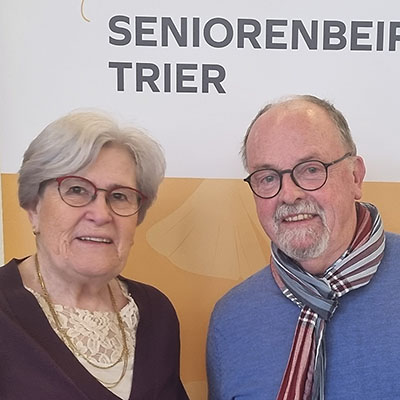 Beide Personen lächeln in die Kamera vor einem Aufsteller mit der Aufschrift "Seniorenbeirat Trier"
